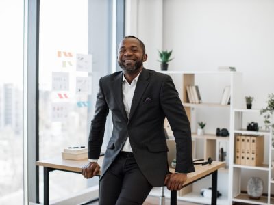 Company leader resting on edge of office desk